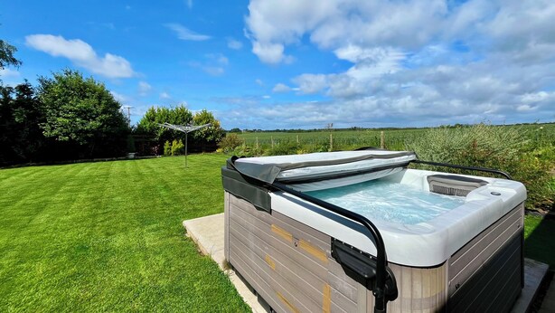 Ein Whirlpool in einem Garten mit Rasen und einem Feld im Hintergrund.