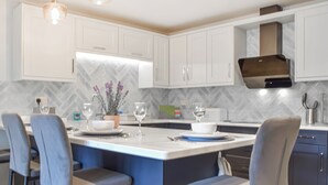A modern kitchen with white cabinets, a central island with bar stools, and pendant lighting.