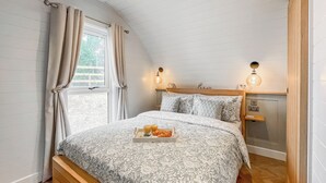 Ein Schlafzimmer mit einem hölzernen Bett, einem Nachttisch mit Lampe und einem Fenster mit Vorhängen.