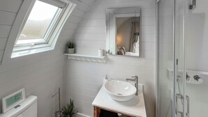 Ein Badezimmer mit Dachfenster, einem weißen Waschbecken, einem Spiegel und einer Dusche.