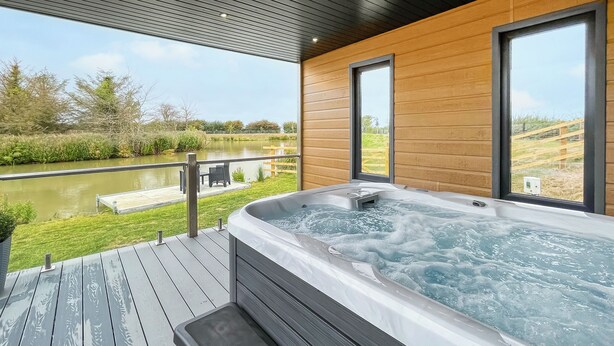 Ein Whirlpool auf einer Holzterrasse mit Blick auf einen See und Gartenmöbeln.