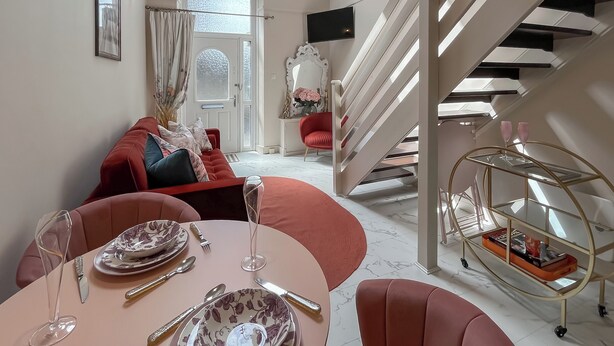 Un coin repas avec une table dressée pour quatre personnes, un canapé rouge, un escalier et un miroir décoratif.
