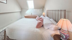 Une chambre à coucher avec un grand lit, une table de chevet, une lampe, un luminaire suspendu, une fenêtre et un radiateur.