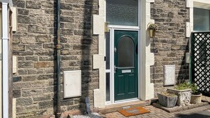 Une maison en pierre avec une porte verte, une fenêtre à cadre blanc et un portail noir.