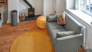 A cozy living room with a grey sofa, a round yellow rug, a fireplace, and a window with curtains. - Roseland Retreat - UK49838 (Truro)