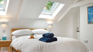 A neatly made bed with white bedding, a skylight above, and a painting on the wall. - Roseland Retreat - UK49838 (Truro)