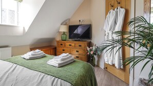 Une chambre à coucher avec un lit, une télévision, une commode en bois et une plante verte.