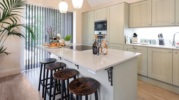 Une cuisine moderne dotée d’un îlot central, de tabourets de bar, de luminaires suspendus et offrant une vue dégagée grâce à de grandes fenêtres.