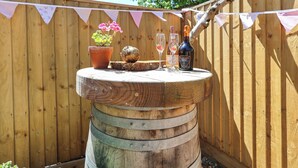 Une table en forme de baril, faite de bois, sur laquelle sont posés un pot de fleurs, deux verres et une bouteille.