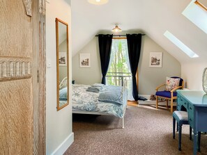 Een slaapkamer met een bed, een bureau, een stoel, een spiegel en een raam met gordijnen.