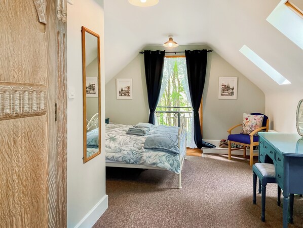 Une chambre à coucher avec un lit, un bureau, une chaise, un miroir et une fenêtre avec des rideaux.