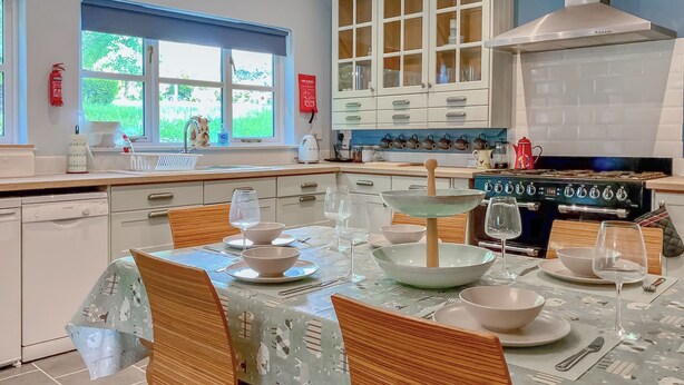 Cozinha moderna com área de jantar, com fogão, armários e janela com vista para o verde.