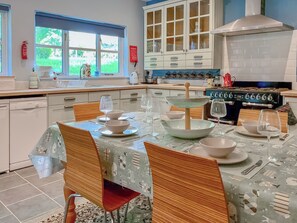 A modern kitchen with a dining area, featuring a stove, cabinets, and a window with a view of greenery.