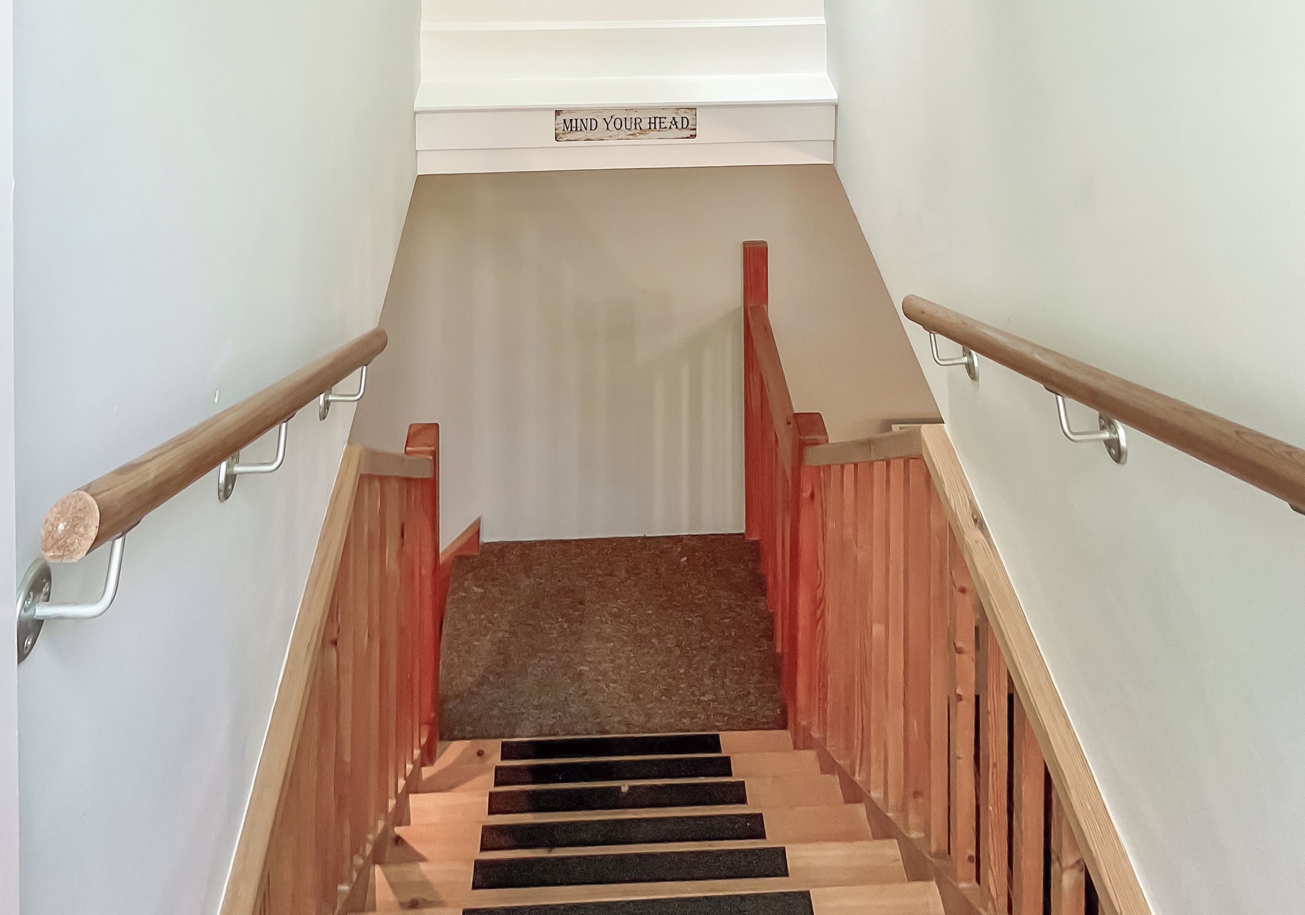 A wooden staircase with metal handrails and a sign that reads "MIND YOUR HEAD".