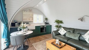 Ein modernes Wohnzimmer mit einem grünen Sofa, einem Holztisch und einem Essbereich mit weißem Tisch und Stühlen.