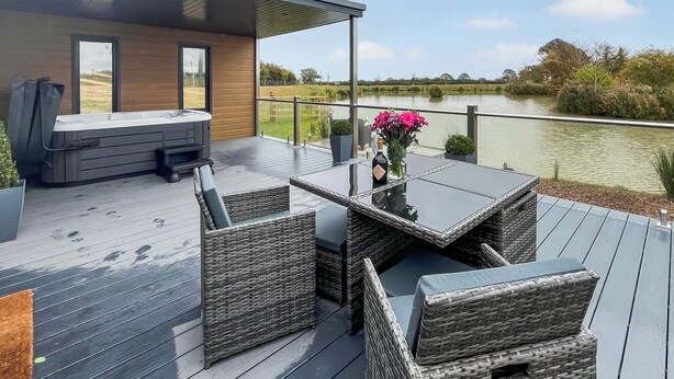 Eine Terrasse mit Korbmöbeln, einem Whirlpool und Blick auf einen See.