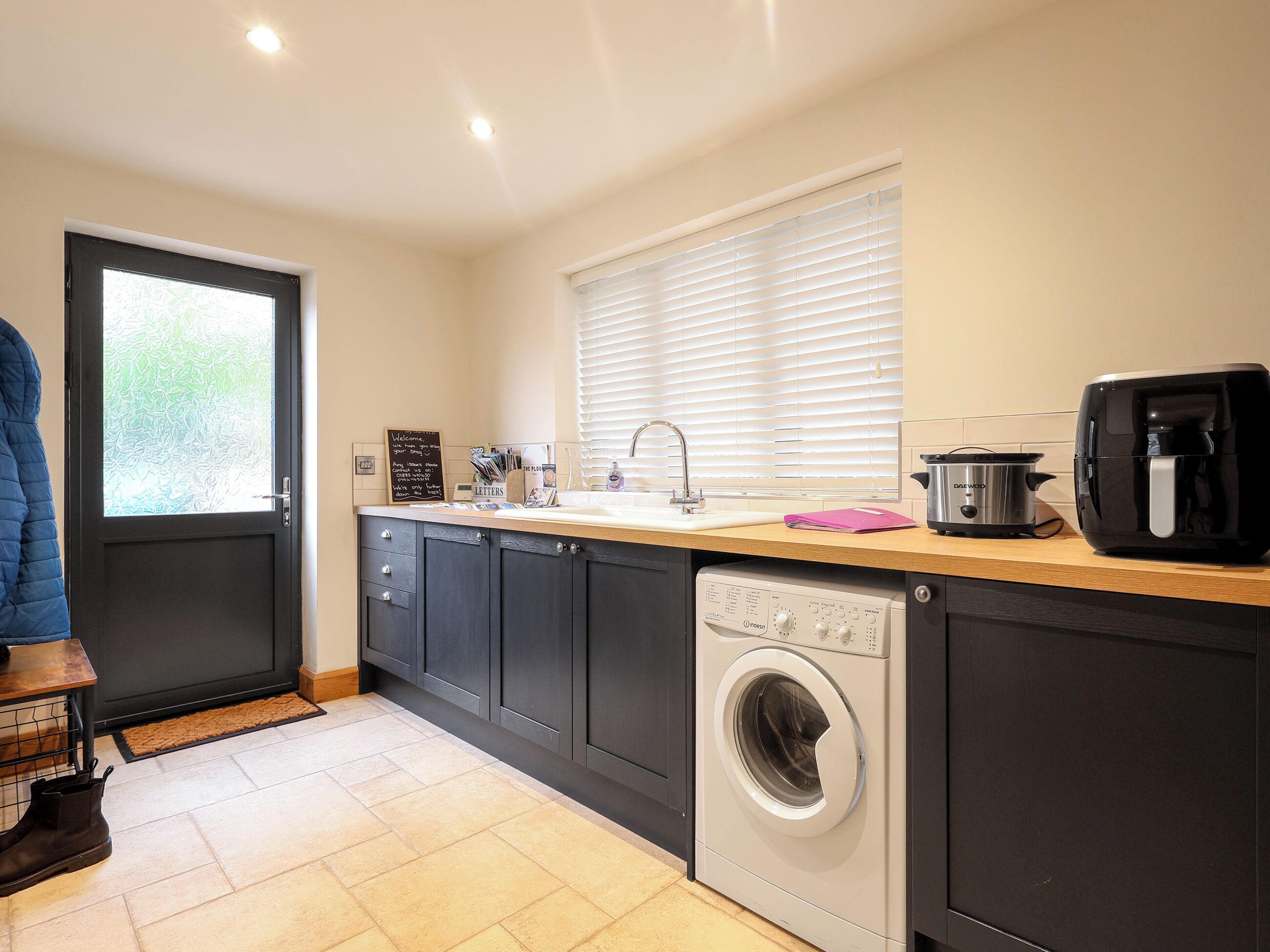 A compact kitchen with a washing machine, a coffee maker, and a window with blinds.