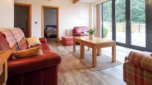 Ein geräumiges Wohnzimmer mit einem roten Sofa, einem Holztisch und Blick auf einen eingezäunten Außenbereich durch große Fenster.