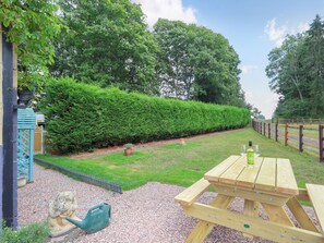 A wooden picnic table with a bottle and a glass, surrounded by a well-maintained lawn and a hedge. - 2 bedroom accommodation in Kyre, near Tenbury Wells (Kyre, near Tenbury Wells)