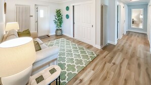 A modern living room with a sofa, a coffee table, a lamp, a patterned rug, a potted plant, and a hallway with wooden flooring. - 4 bedroom accommodation in Perth (Perth)