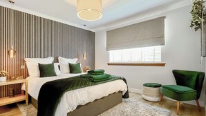 A modern bedroom with a bed, bedside tables, a green chair, a window with blinds, and a hanging light fixture. - 4 bedroom accommodation in Perth (Perth)