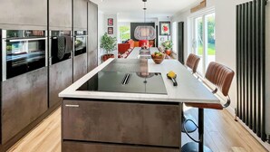 A modern kitchen with a central island, built-in appliances, and a dining area with chairs and a table. - 4 bedroom accommodation in Perth (Perth)