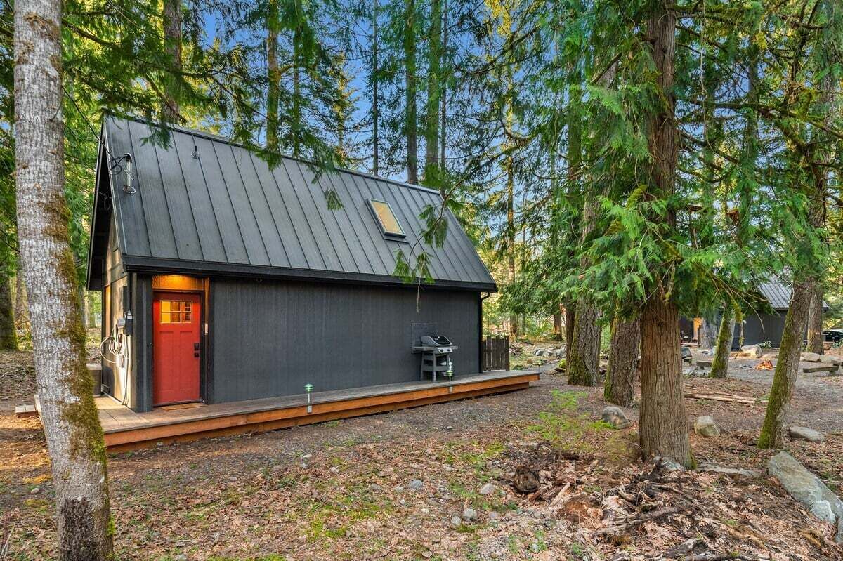 A modern cabin with a red door, a small deck, and a chimney.
