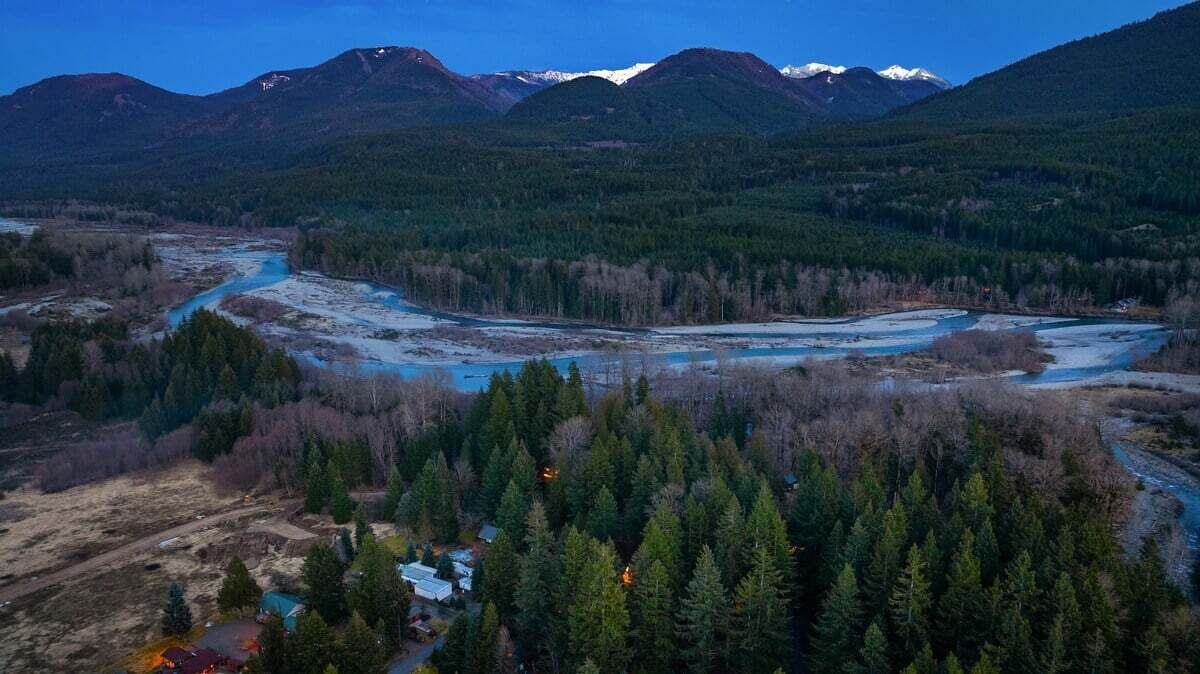 A mountainous landscape with a river, dense forest, and a small settlement with buildings and a road.