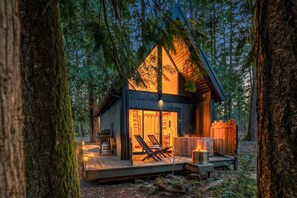 A cozy cabin with a wooden exterior, a deck with lounge chairs, and a fire pit. - Kodiak Cabin | Hot tub, EV, AC (packwood)