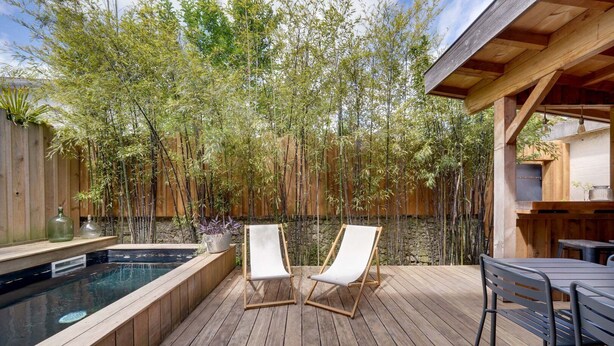 Une terrasse en bois avec un jacuzzi, deux chaises longues et une table avec des chaises.