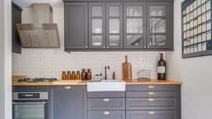 Une cuisine avec des meubles de couleur sombre, une hotte de cuisinière en acier inoxydable, un four encastré et une bouteille de vin posée sur le comptoir.