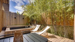 Une terrasse en bois avec un jacuzzi, deux chaises longues et une table agrémentée d’un élément décoratif en fibres tressées.