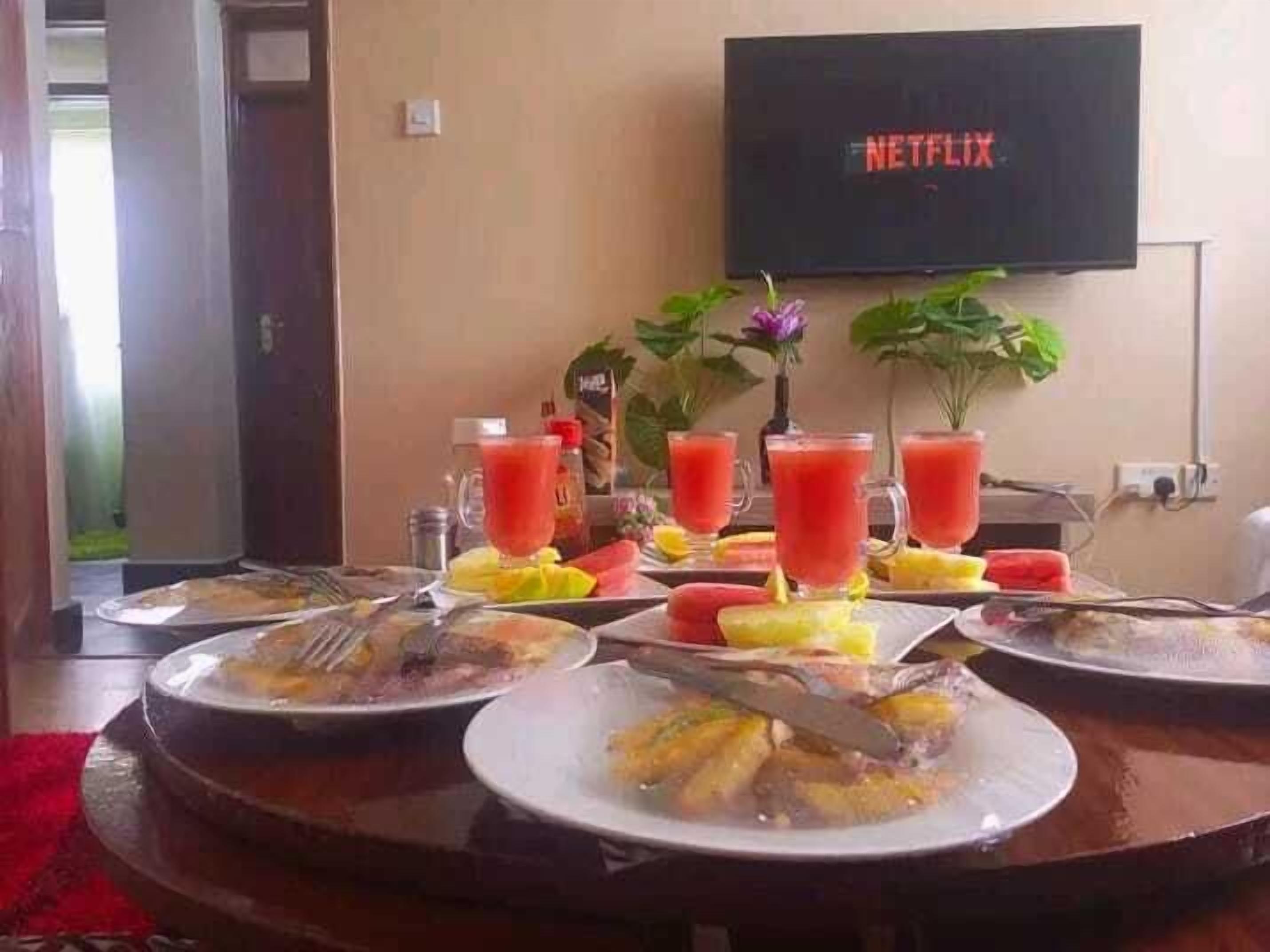 A breakfast table with plates of food, drinks, and a TV displaying 'NETFLIX'.
