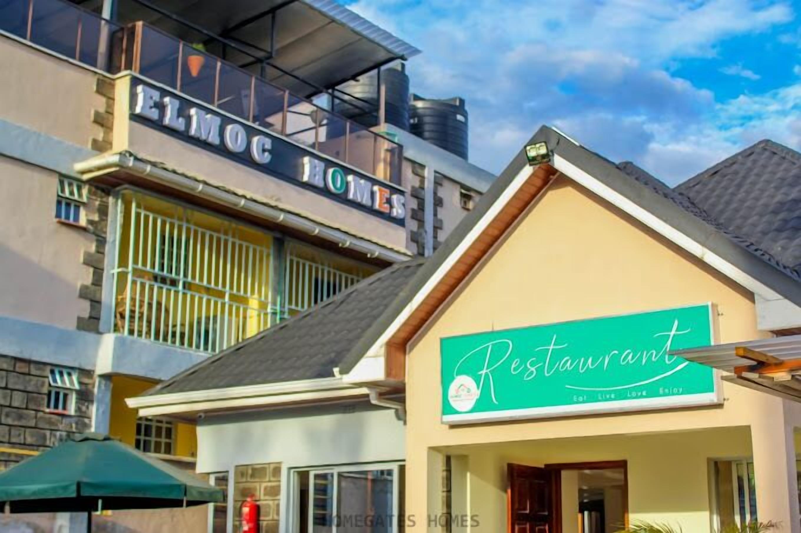 Un bâtiment avec une enseigne indiquant « ELMOG HOMES » et une autre pour un restaurant.