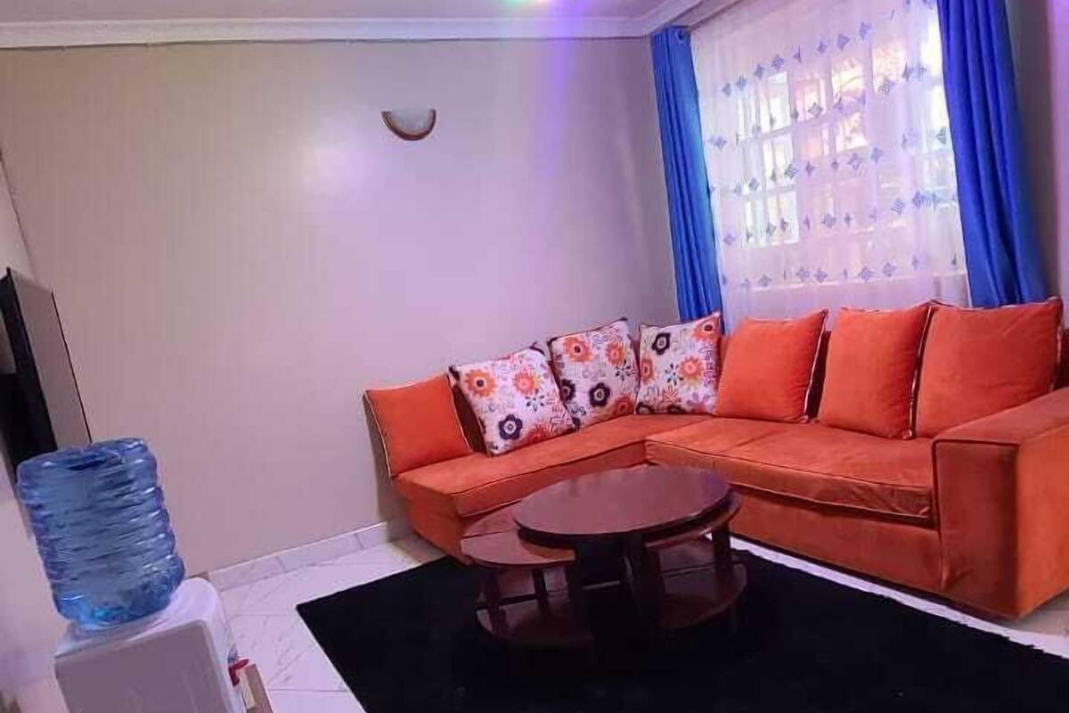 Una sala de estar con sofá, mesa de centro, dispensador de agua y lámpara de techo.