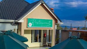 A restaurant with a green sign, outdoor seating with umbrellas, and a view of the mountains. - Lux Suites Elmoc Apartments Nakuru (Nakuru)