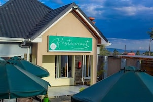 Un restaurante con un letrero verde, mesas al aire libre con sombrillas y vistas a las montañas.