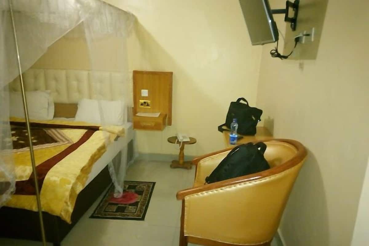 Een hotelkamer met een bed, een stoel, een klein tafeltje, een waterfles en een tv aan de muur.