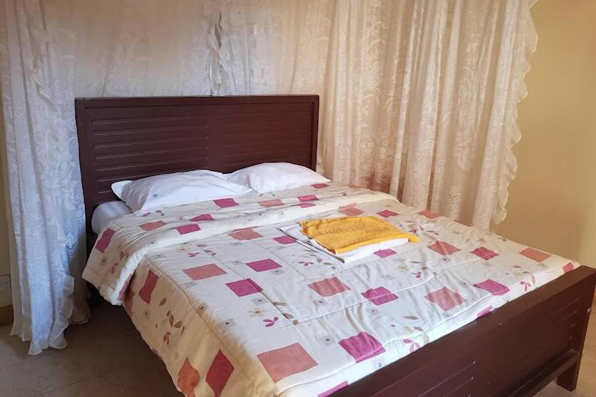 Een bed met een houten hoofdbord, een beddengoed met een patroon en een gele deken.