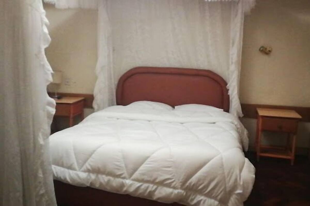 Een eenpersoonsbed met een witte quilt, een houten hoofdbord en twee nachtkastjes.
