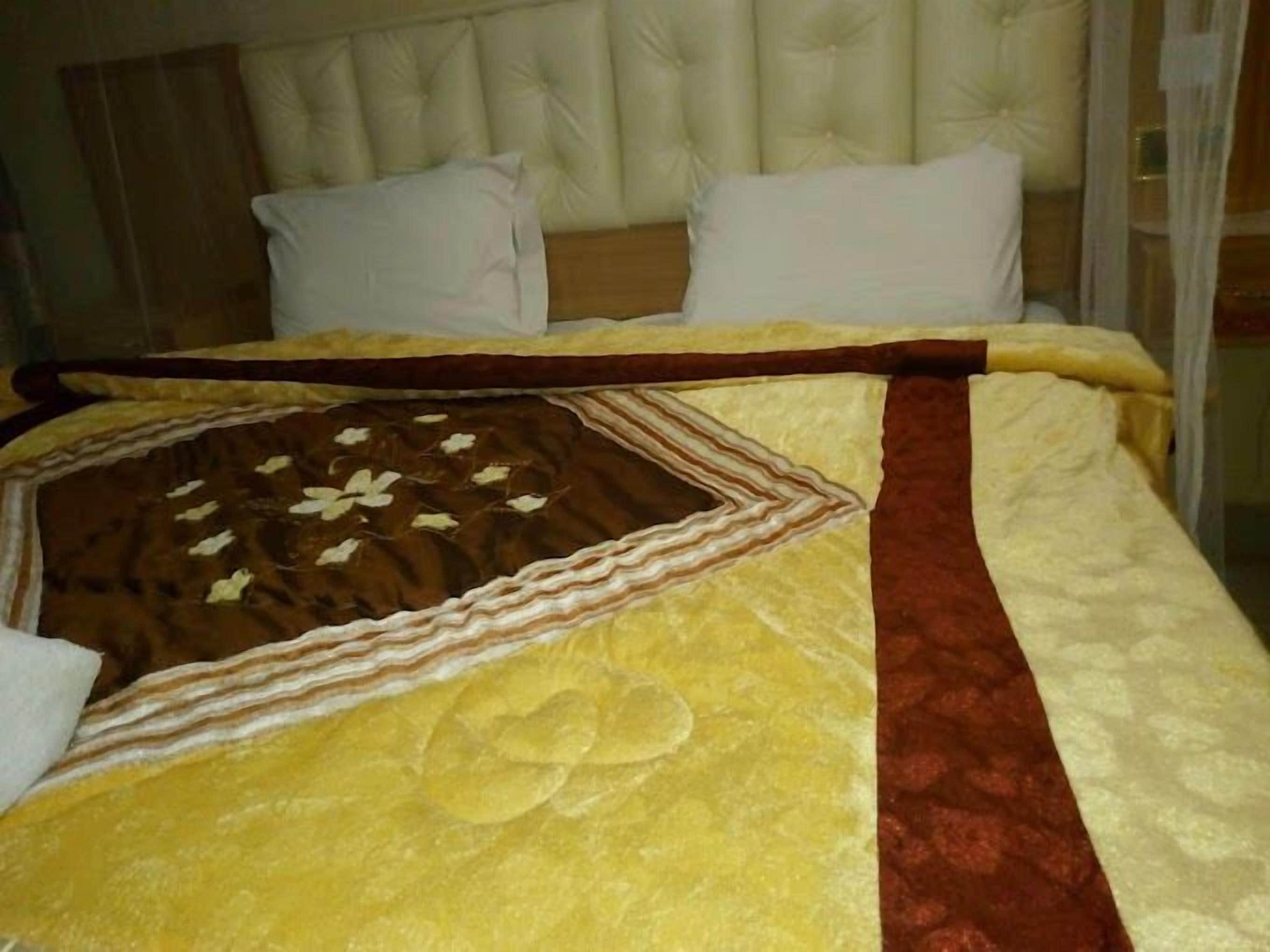 A bed with a quilted headboard, white pillows, and a decorative pillow with a chocolate design.
