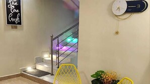 Ein Wohnzimmer mit Treppe, zwei gelbe Sessel, einer Uhr und einem motivierenden Spruch.