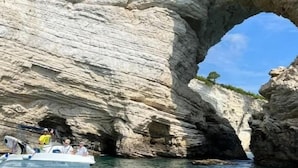 A boat near a large rock arch with clear water. - B&B La Munachell  (Vieste)