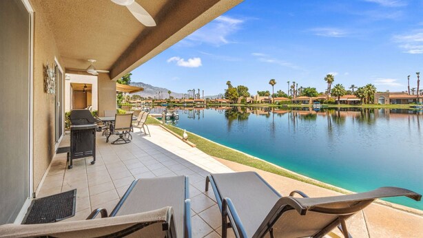 Zona junto a la piscina con sillones de descanso, una parrilla y vista a un lago y edificios a la distancia.