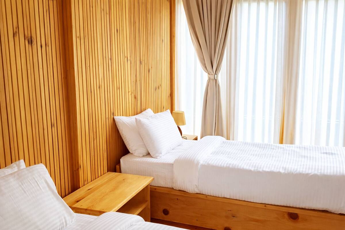 Una habitación con paneles de madera, una cama, una mesita de noche y cortinas.