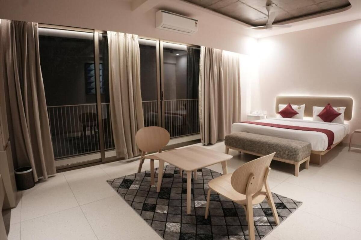 Ein Hotelzimmer mit einem Bett, einem Nachttisch, einem Sessel, einem kleinen Tisch und Blick durch eine Schiebetür nach draußen.