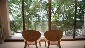 Two wooden chairs facing a balcony with a view of trees and a railing. - Riverscapes By Noorjehan (Palakkad)
