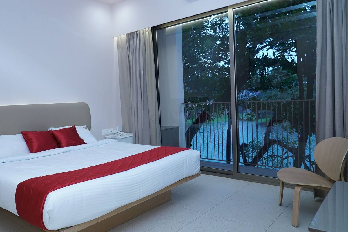 Ein modernes Hotelzimmer mit einem großen Bett, einem Holzstuhl und Blick auf einen Balkon mit Geländer.