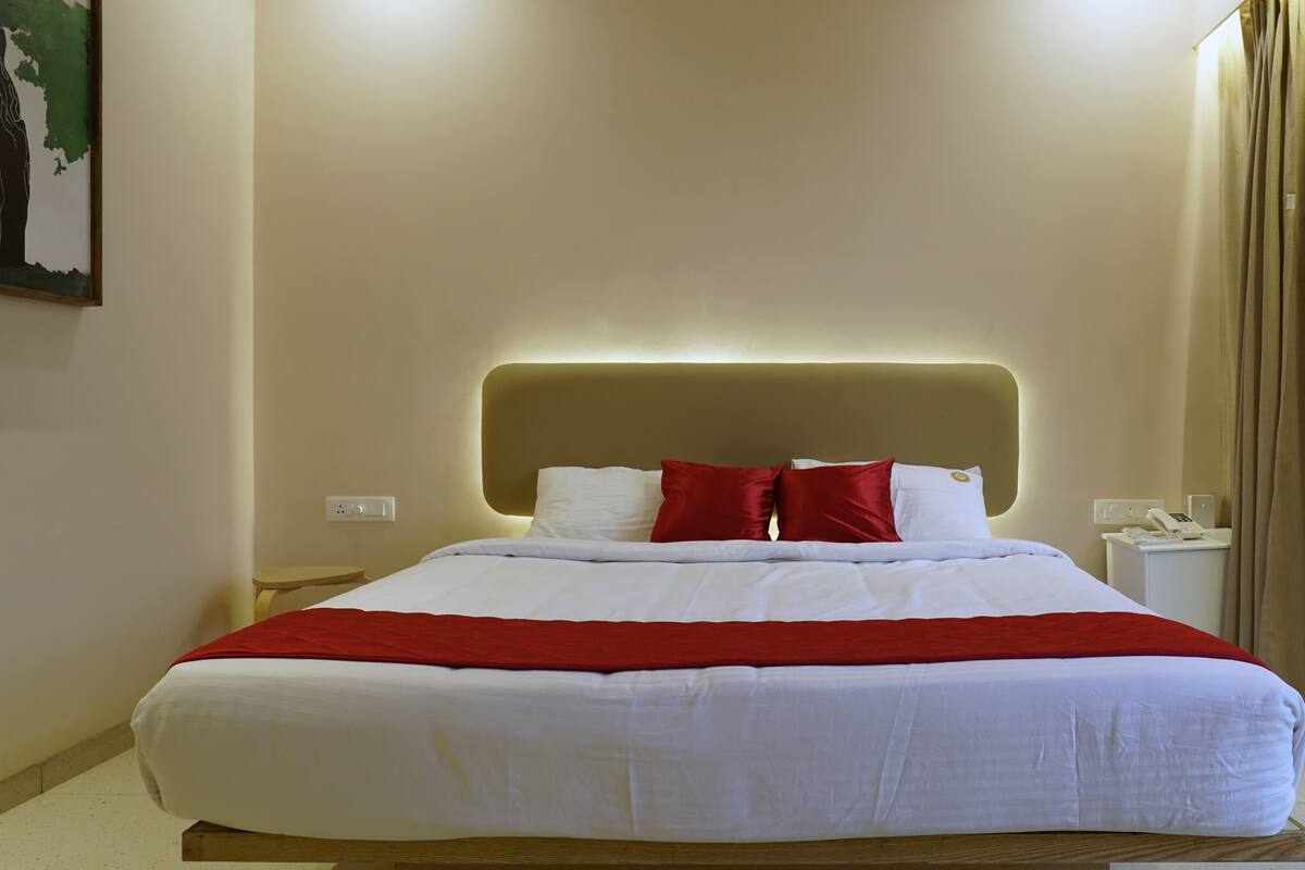 Ein ordentlich bezogenes Bett mit weißer und roter Bettwäsche, ein moderner Kopfteil, Nachttische mit einem Telefon und ein Gemälde an der Wand.
