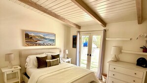 A bedroom with a bed, bedside tables, a dresser, a bench, a painting, and a door leading outside. - Montectio Magic (Montecito)